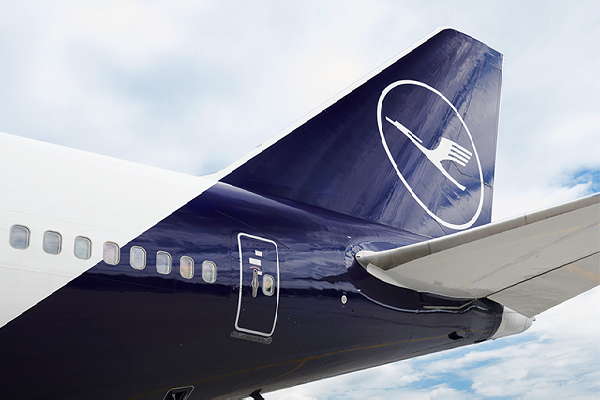 En la cola y el alerón trasero de un avión de pasajeros, ambos de color azul, se puede ver el logo de la aerolínea Lufthansa, en color blanco.